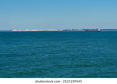 A large ship sailing across calm blue waters with a distant shoreline in Cádiz under a clear sky, highlighting a serene coastal scene and peaceful maritime setting - Powered by Shutterstock