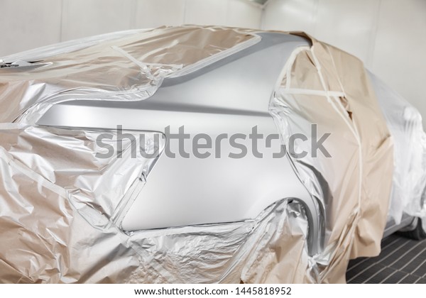 A large silver sedan car is completely covered\
in paper and adhesive tape to protect against splash during\
painting after an accident in a workshop for body repair of\
vehicles. Auto service\
industry.