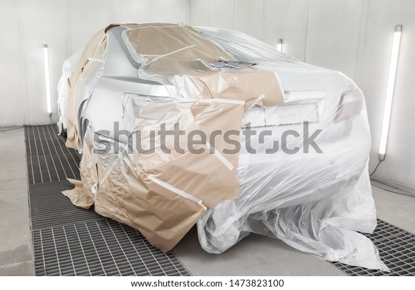 A large silver sedan car is completely covered\
in paper and adhesive tape to protect against splash during\
painting after an accident in a workshop for body repair of\
vehicles. Auto service\
industry.