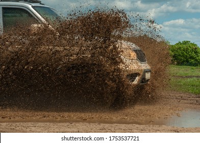 Large silver SUV is off roading in the mud in the highlands on a sunny summer day. 4X4 in the mountains. Four-wheel drive, low gear on dirt road, mud, spray.