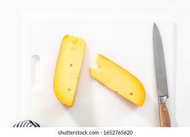 Large Slice Of Smoked Gouda Cheese On A White Cutting Board.