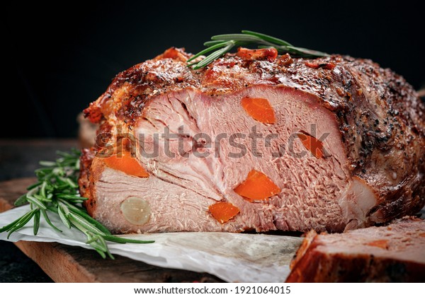 Large sliced piece of baked pork tenderloin\
with seasonings on a wooden kitchen\
board