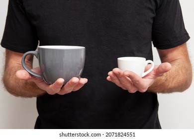 Large And Small Cups In Male Hands. Comparison Concept. Choosing The Right Size. Diverse Offer.