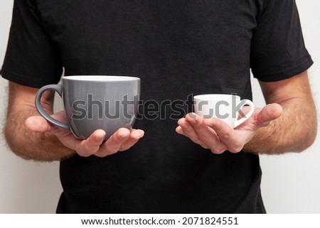 Large and small cups in male hands. Comparison concept. Choosing the right size. Diverse offer.