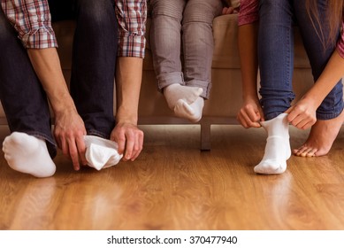 Large And Small Feet. Family Sitting On Sofa Together - Focus On Feet. Family's Feet Close-up On Wood Floor.