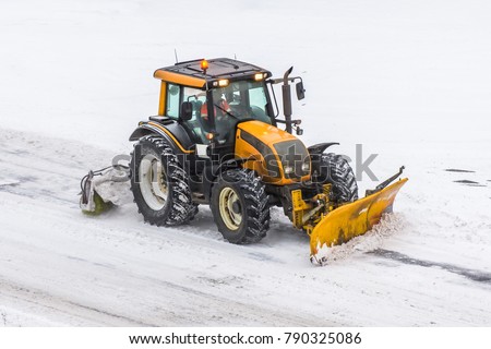 Large snow plowing tractor machine at work on the road during a snow storm in winter