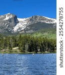 Large snow tipped mountains above a green tree line. Fly fishers  spread out in the blue, Sprague lake. Colorful Colorado. Rocky Mountain National Park. 