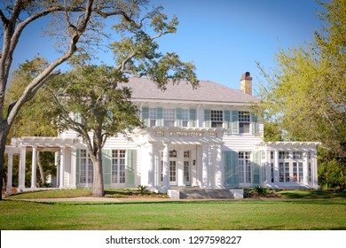 Large Southern Style Home In America Featuring Large Windows, Shutters And A Porch. Oak Trees Frame The Exterior Of The House.