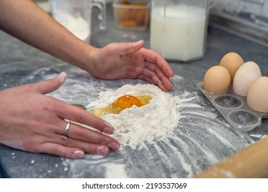 At A Large Spacious Table A Woman Prepares Dinner Where She Breaks Eggs And Kneads Dough For Casserole. Cooking Concept