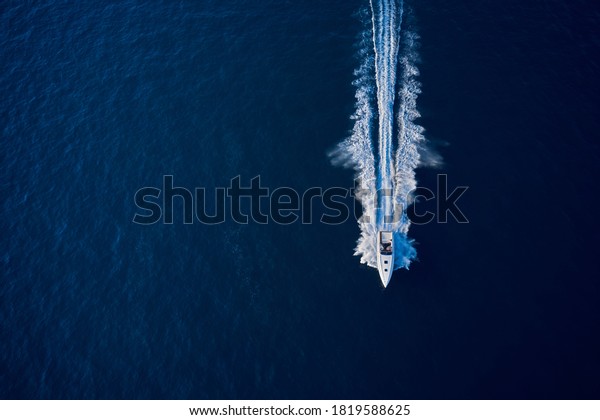 Large speed boat moving at high\
speed. Top view of a white boat sailing to the blue sea. Drone view\
of a boat sailing. Motor boat in the sea. Travel -\
image.