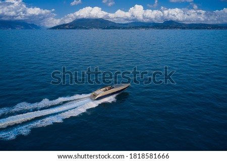 Large speedboat moving at high speed in the background of the coastline mountains and cumulus clouds. The boat is gray-blue combined color. Large speed boat moving at high speed side view.
