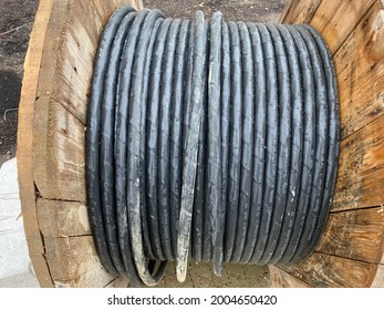 Large Spool With Black Thick Electrical Wire Or Cable. Wooden Coil With Electrical Industrial Wires At A Construction Site.