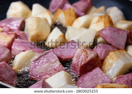 Large square chunks of white and pink potatoes (red Pontiac variety) are cooked on oil in a frying pan, getting crusty.