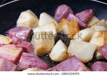 Large square chunks of white and pink potatoes (red Pontiac variety) are cooked on oil in a frying pan, getting crusty.