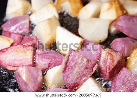 Large square chunks of white and pink potatoes (red Pontiac variety) are cooked on oil in a frying pan, getting crusty.