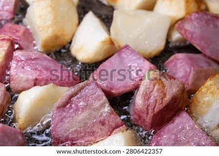 Large square chunks of white and pink potatoes (red Pontiac variety) are cooked on oil in a frying pan, getting crusty.