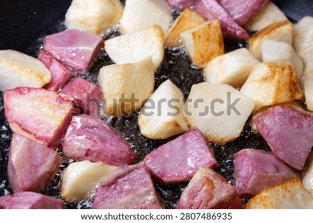 Large square chunks of white and pink potatoes (red Pontiac variety) are cooked on oil in a frying pan, getting crusty.