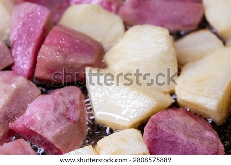 Large square chunks of white and pink potatoes (red Pontiac variety) are cooked on oil in a frying pan, getting crusty.