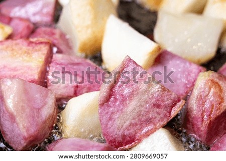 Large square chunks of white and pink potatoes (red Pontiac variety) are cooked on oil in a frying pan, getting crusty.
