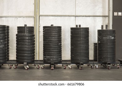 A large stack of barbell plates stacked on movable pegs on wheels in a gym waiting to be used 