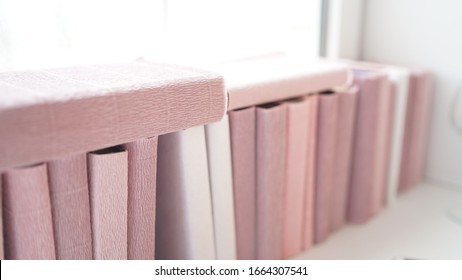 Large stack of books on windowsill. Books wrapped in colored paper lie on window sill.