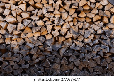 Large stack of chopped dry firewood logs piled together with light and dark color gradient for winter heating fuel