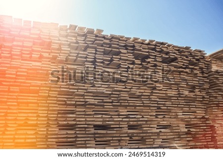 A large stack of lumber boards is neatly stacked at a lumber yard. The boards are arranged in a uniform pattern, with the grain running vertically