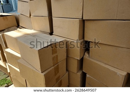 Large stack of plain cardboard boxes used for packaging, shipping, or storage outdoors in daylight. Ideal for logistics, delivery, or warehouse themes.
