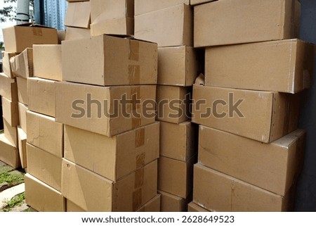 Large stack of plain cardboard boxes used for packaging, shipping, or storage outdoors in daylight. Ideal for logistics, delivery, or warehouse themes.