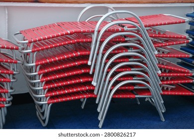 A large stack of red plastic strap sun loungers with aluminum frames stored neatly on a blue cruise ship deck