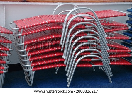 A large stack of red plastic strap sun loungers with aluminum frames stored neatly on a blue cruise ship deck