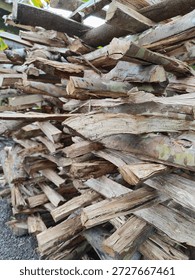 ​A large stack of split logs and firewood is piled neatly outdoors The varying textures of the bark and raw wood create a rustic, natural scene in a rural setting