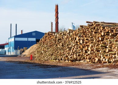 A Large Stack Of Timber Waiting To Be Turned Into Biofuel. Heating Plant In Background.