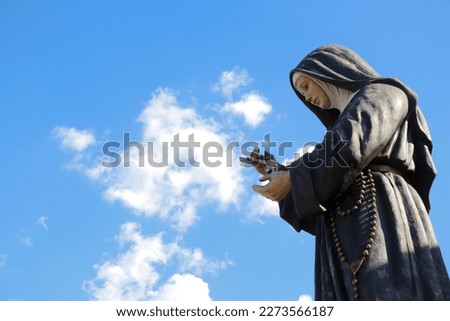 Large statue of saint rita de cassia with blue sky and clouds in the background