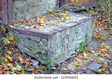 a large step of a gray concrete threshold with a brown iron corner on the ground in fallen dry leaves on the street