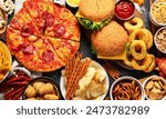 Large table of assorted take out food such as pizza, french fries, onion rings, burgers and snacks on a dark background. Top view.