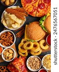Large table of assorted take out food such as pizza, french fries, onion rings, burgers and snacks on a dark background. Top view.