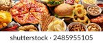 Large table of assorted take out food such as pizza, french fries, onion rings, burgers and snacks on a dark background. Top view. Panorama, banner.