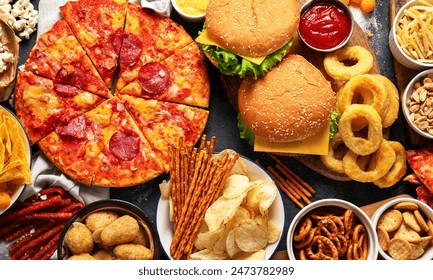 Large table of assorted take out food such as pizza, french fries, onion rings, burgers and snacks on a dark background. Top view. - Powered by Shutterstock