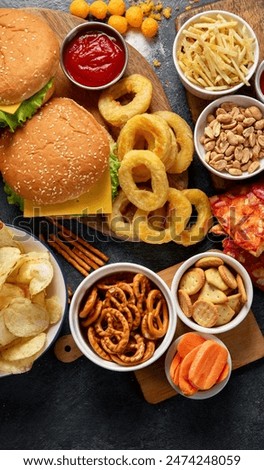 Large table of assorted take out food such as pizza, french fries, onion rings, burgers and snacks on a dark background. Top view.