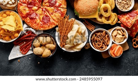 Large table of assorted take out food such as pizza, french fries, onion rings, burgers and snacks on a dark background. Top view. Panorama with copy space.
