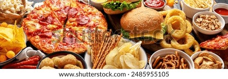 Large table of assorted take out food such as pizza, french fries, onion rings, burgers and snacks on a dark background. Top view. Panorama, banner.