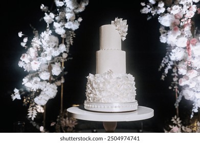 Large tall decorated white three-tiered wedding cake stands on wooden table stand at night against arch background. Food photography, sweet dessert. - Powered by Shutterstock