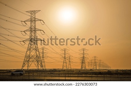 Large tall steel power pylons in rather flat landscape of Saudi Arabia, only black silhouettes visible against bright afternoon sun