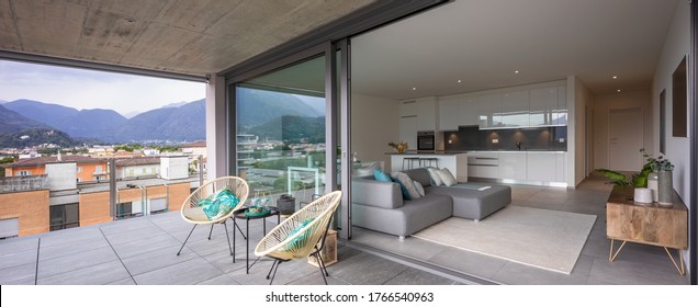 Grosse Terrasse mit zwei Sesseln oder Stühlen. Sie können auch das Interieur des modernen Apartments mit seiner offenen Küche und seinem Wohnzimmer oder Wohnzimmer sehen.