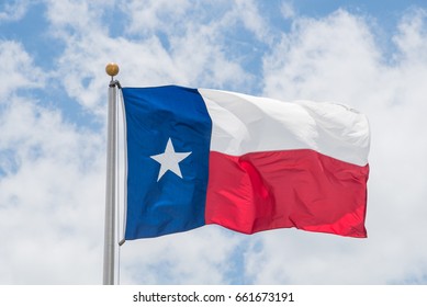 Large Texas (The Lone Star) flag waving on flag pole with cloud blue sky. Windy and sunny day with waving flag blowing/flowing. Ruffled Texas flag. Room for text, copy space.