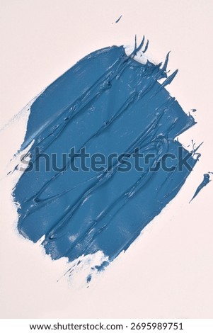 A large, textured, rectangular swipe of thick, matte blue paint is diagonally placed on a white surface