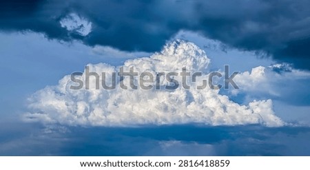 Large thundercloud during downpour is suddenly illuminated by sun. White clouds of steam smoke large mountain atmospheric volume, detailed explosion of precipitation. An oppressive, dark atmosphere.
