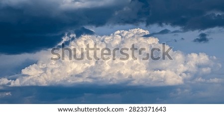 Large thundercloud during downpour is suddenly illuminated by sun. White clouds of steam smoke large mountain atmospheric volume, detailed explosion of precipitation. An oppressive, dark atmosphere.