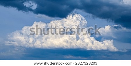 Large thundercloud during downpour is suddenly illuminated by sun. White clouds of steam smoke large mountain atmospheric volume, detailed explosion of precipitation. An oppressive, dark atmosphere.